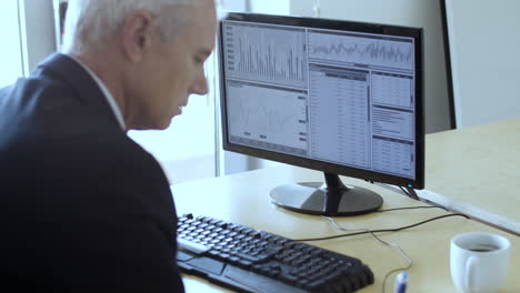 focused grey haired male trader analyzing financial charts