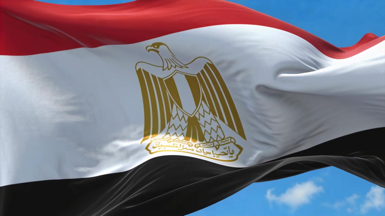 Vlající egyptská národní vlajka reagující na nárazový vítr na modré obloze, odhalující zlatý emblém orla.