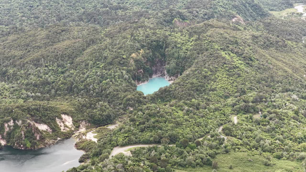 Órbita de dron revelando un lago de cráter escondido en el denso bosque del Valle Volcánico de Waimangu, Nueva Zelanda, rodeado de árboles forestales, vista geográfica
