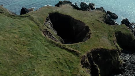 Aerial-closeup-of-small-hole-near-cliff-by-the-sea-at-day-in-summer