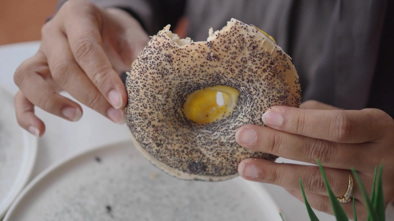 Person Holding a Poppy Seed Bagel with a Fried Egg Center