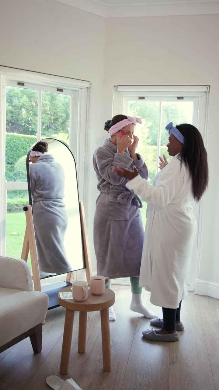 Vertical video: Diverse female friends applying mask wiping sipping coffee and dancing at home