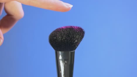un dedo toca un pincel cosmético de brillo rosado en cámara lenta.
