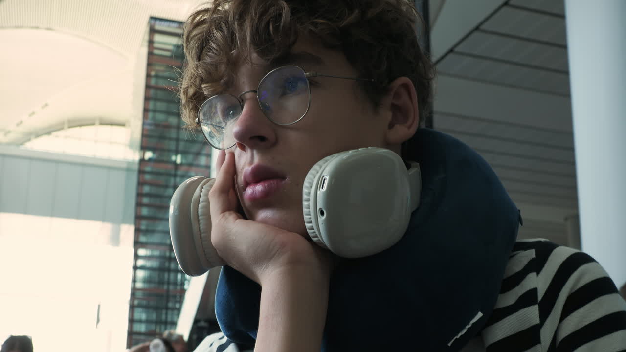 Giovane Uomo con Cuffie e Cuscino da Viaggio in Attesa in Aeroporto.