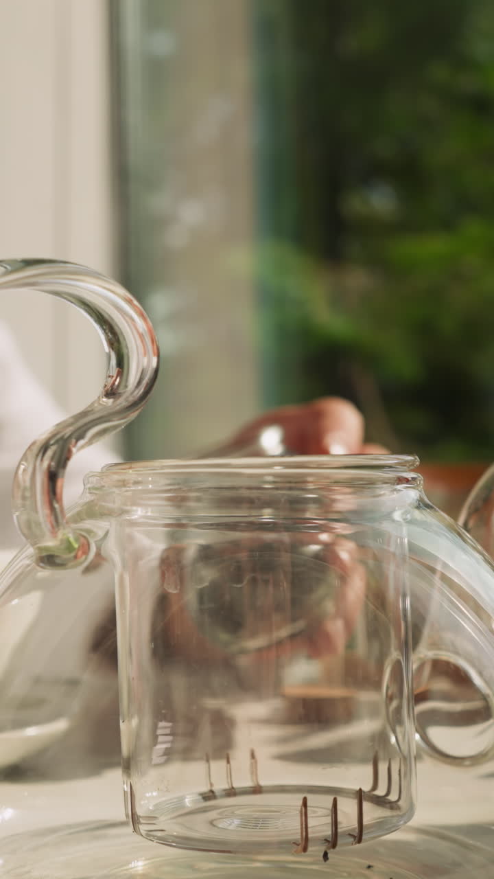 el hombre abre la tapa de una elegante tetera de vidrio para preparar té. el joven disfruta de la ceremonia del té todas las mañanas. el hombre prefiere la mezcla de té natural para la bebida matutina