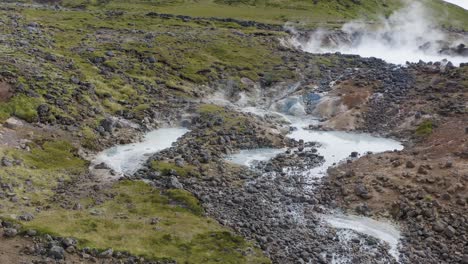 aerial approaching shot of olkelduhals geothermal area with sulfur lakes and mud pots in iceland - fumes ascending into sky