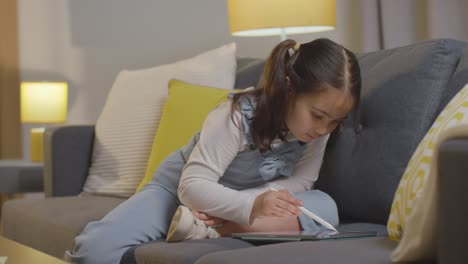 niña en casa sentada en un sofá dibujando en una tableta digital con lápiz óptico 1