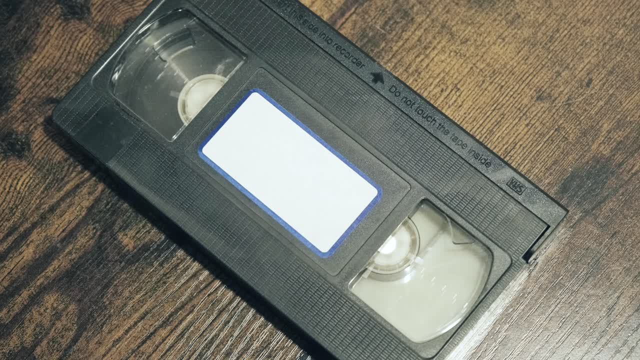 manos pegando una etiqueta en blanco en el lado delantero de una cinta de vhs vintage