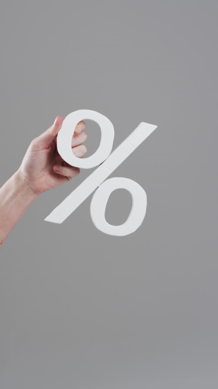 Vertical video of hand of caucasian woman holding percent sign with copy space on grey background
