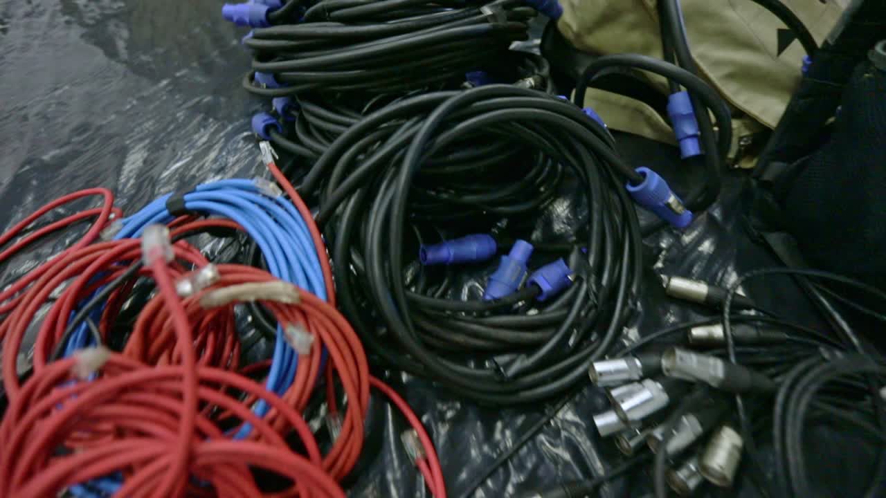 montón de cables agrupados en un estudio de transmisión de televisión mientras un equipo prepara el escenario