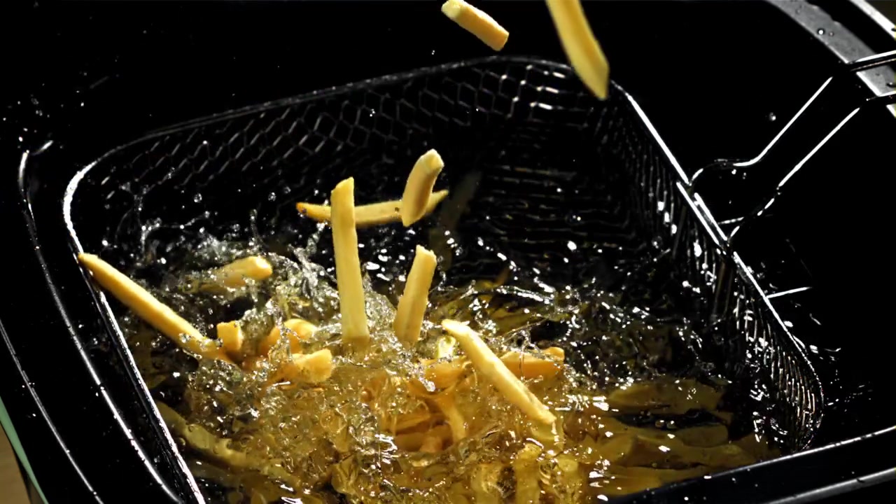 Sakte film av pommes frites som faller ned i varm olje i en frityrkoker