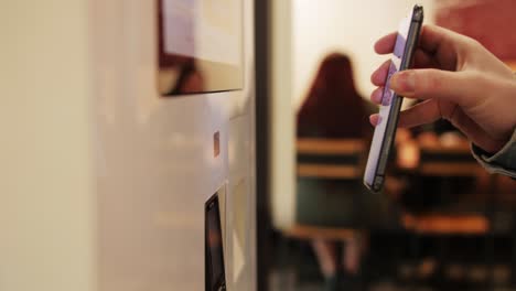 a man is using his smartphone for a digital payment transaction at a selfservice kiosk in a modern cafe environment