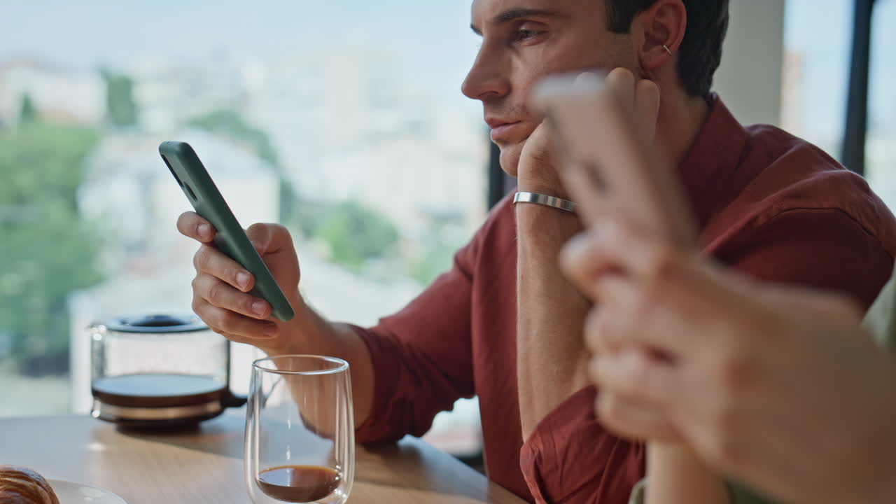 Couple hands holding smartphones sitting kitchen table with coffee cup closeup