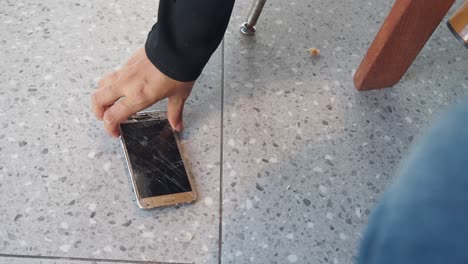 persona recoge un teléfono roto del suelo