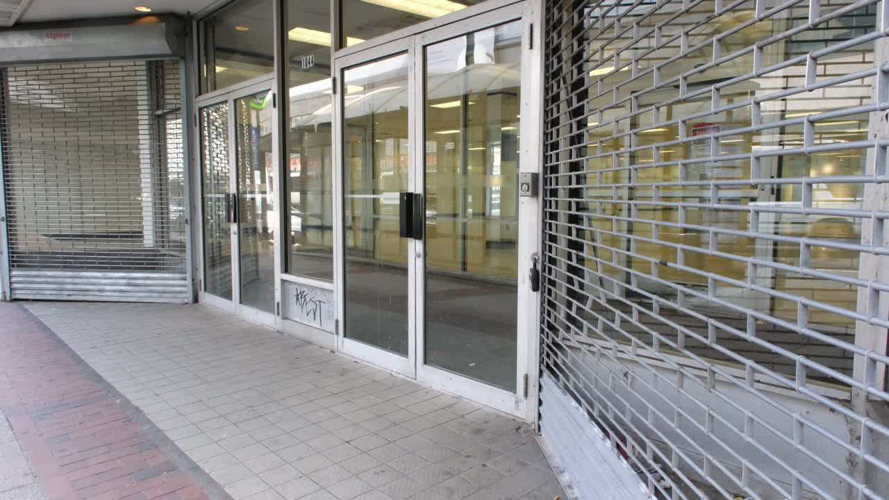 A closed storefront with glass doors, metal security gate, and graffiti in Market East, Philadelphia.