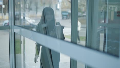 professional female manager in a black formal outfit, walking through the office, interacting with colleagues, holding documents and a laptop, showcasing leadership and professionalism