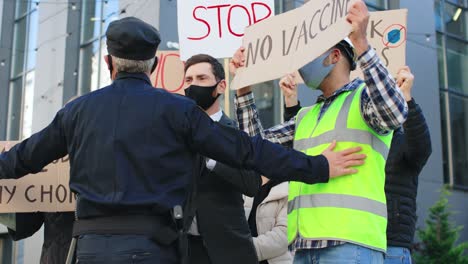 policjant zatrzymuje grupę ludzi w demonstracji przeciwko covidowi 19 na ulicy