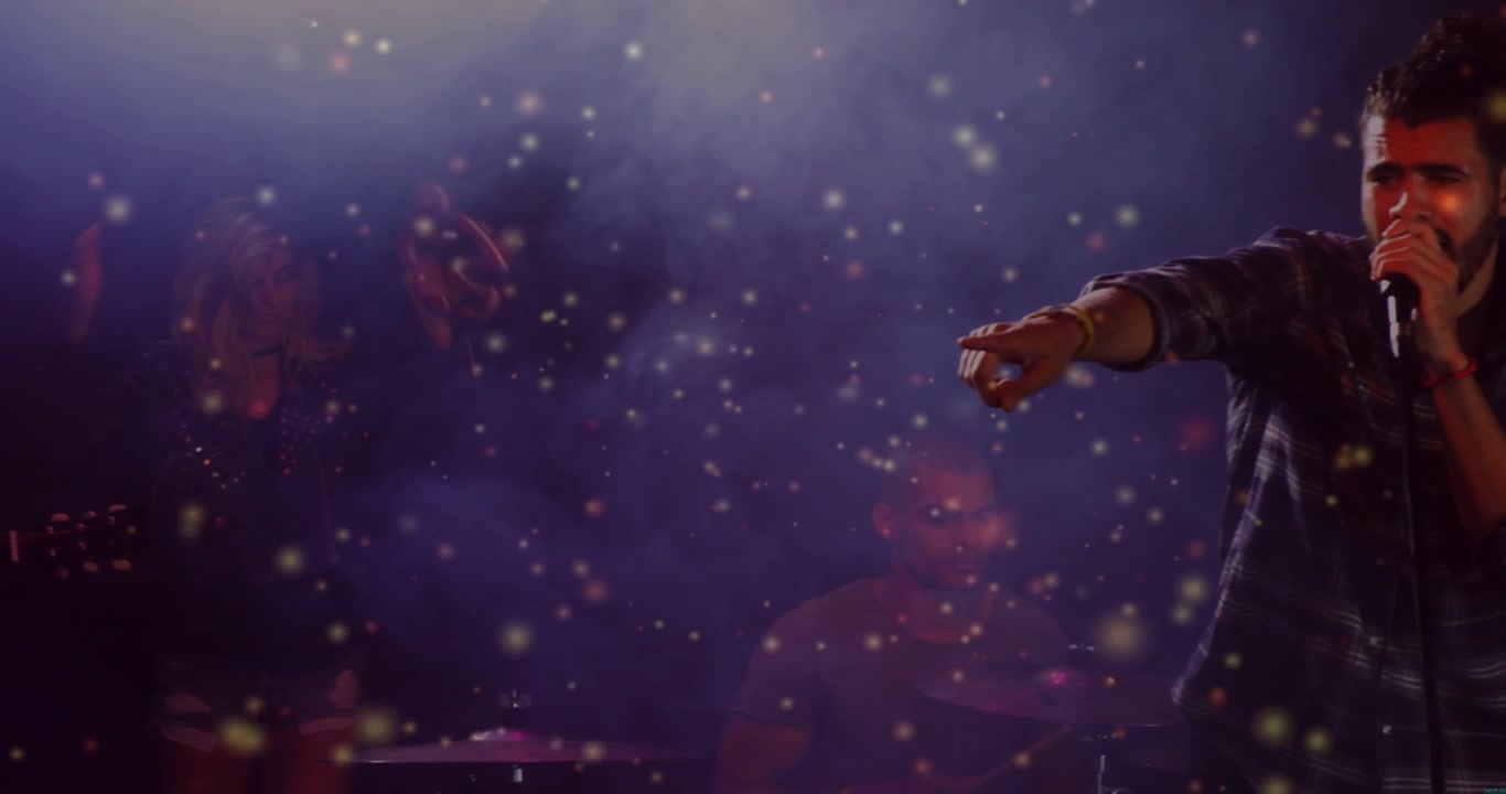 Lead vocalist stepping inward, performing to engage crowd in music, drawing sparkles over drum kit