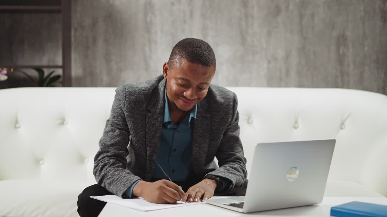 African-American student writes notes at laptop at home