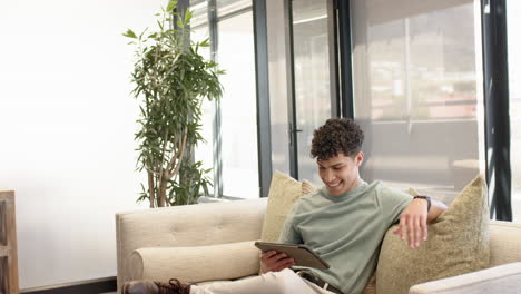relaxing on couch, man using tablet in modern living room with large windows, at office