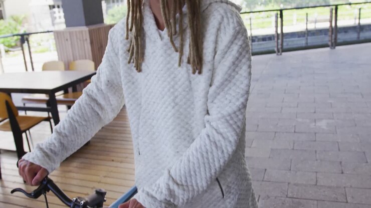 Uomo di etnia mista con i dreadlock che spinge una bicicletta a mano per strada