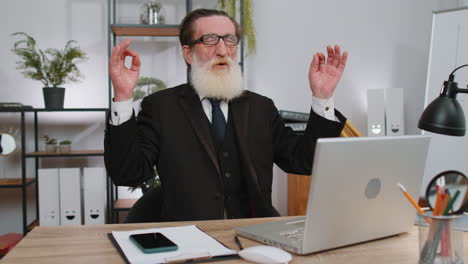 hombre de negocios trabajando en una computadora portátil, meditando, haciendo ejercicios de respiración de yoga en posición de loto en la oficina