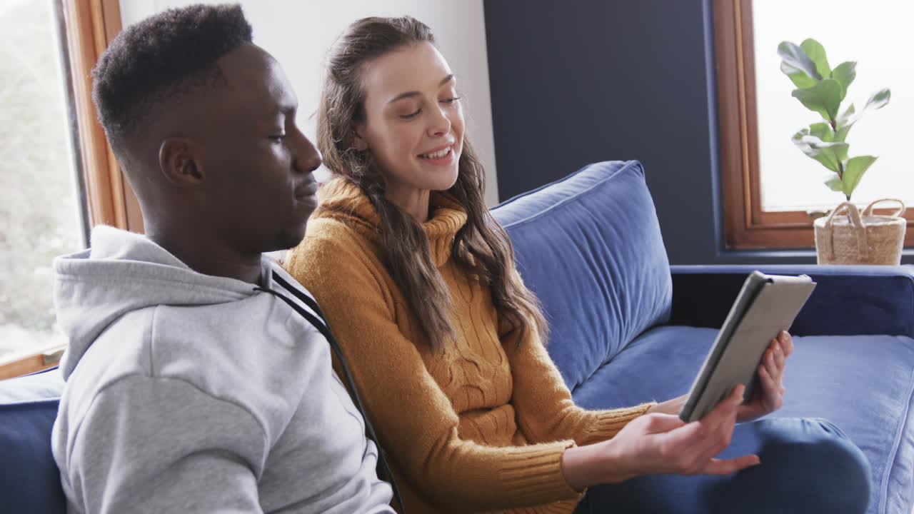pareja feliz sentada en el sofá y usando la tableta en el hogar, espacio de copia