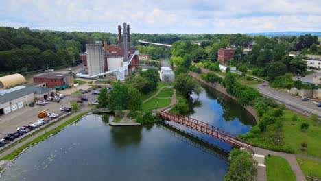 aerial drone footage of the river walk park, the chadakoin river, and an industrial area of downtown jamestown, new york, during summer with a pedestrian bridge