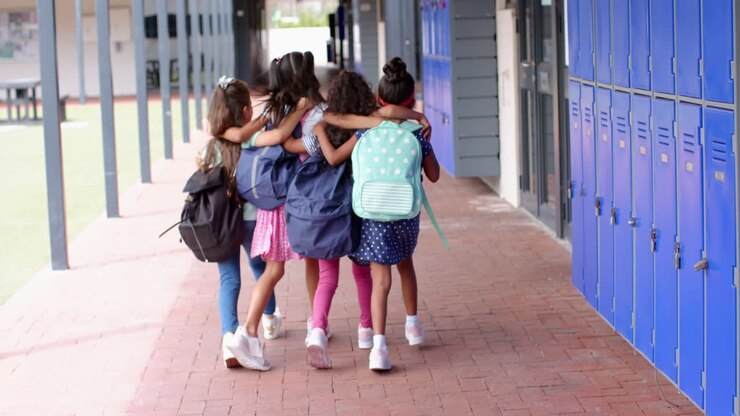Grupo de colegialas caminando juntas con mochilas en el pasillo de la escuela