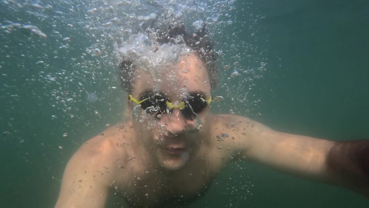 Uomo con occhialini che soffia molte bolle mentre nuota sott'acqua durante l'estate, rappresentando il tempo libero, lo sport e la libertà.