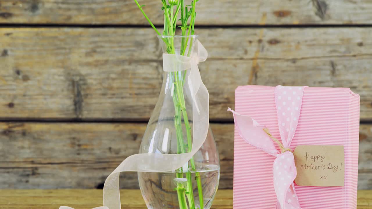 caja de regalos y jarrón de flores en superficie de madera