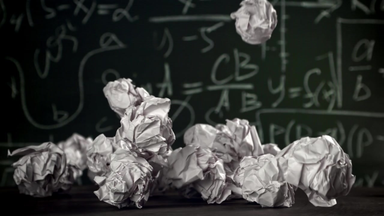 Crumpled Paper Balls Falling in Slow Motion Against a Chalkboard with Math Formulas