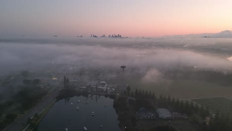 Aerial-video-of-foggy-Sydney-suburb-with-city-view-at-horizon,-Australia-at-sunrise