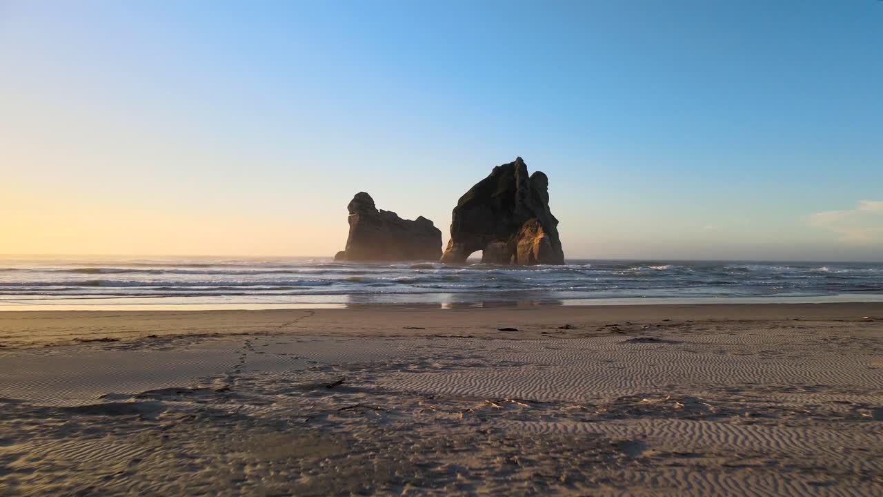 hermoso plano aéreo pintoresco de la playa de wharariki y un joven turista con cámara disfrutando de la naturaleza