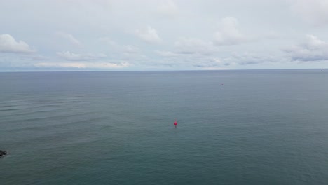 A-breathtaking-aerial-view-of-the-vast-ocean-with-a-visible-red-buoy-and-rock-breakwater,-capturing-the-beauty-and-power-of-nature