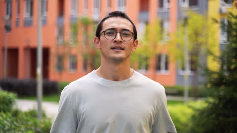 outdoor portrait of a happy japanese young man wearing eyeglasses smiling and walking towards camera 1