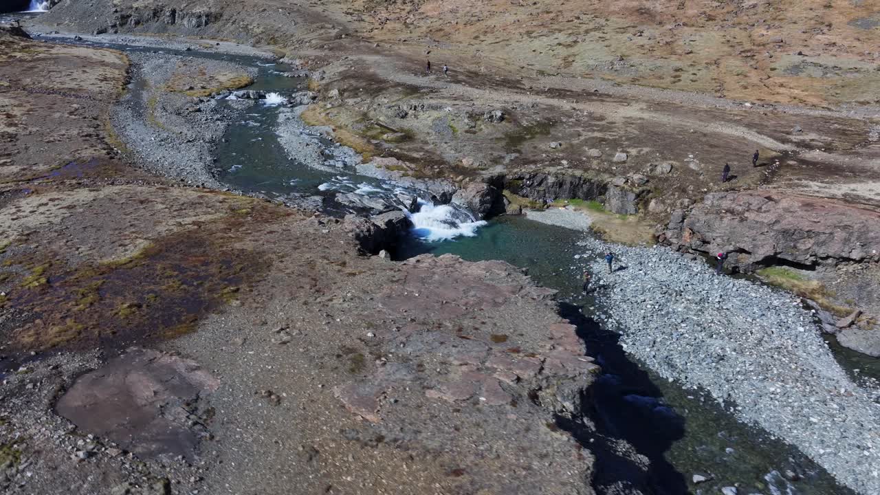 un dron se desliza por encima de la zona, capturando imágenes de la pintoresca cascada skutafoss donde se ven pocas personas apreciando su belleza
