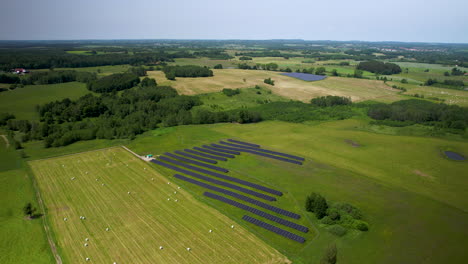 aerial drone over solar panels in field next to farmland, lush green