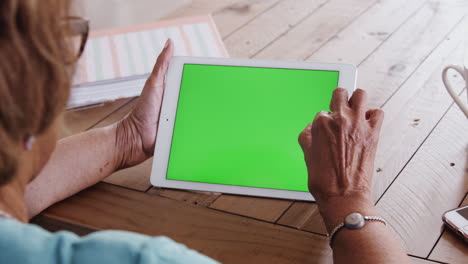 Senior-black-woman-at-a-table-using-a-tablet-computer-horizontally,-over-shoulder-view,-close-up