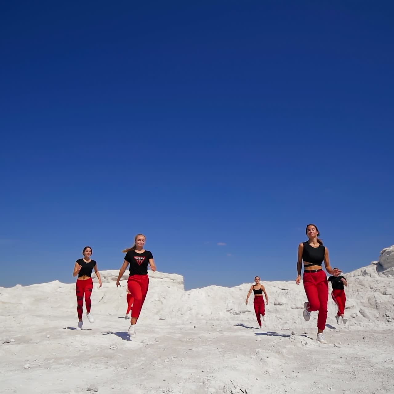 Young sportive girls wearing similar outfit run by the white rocky ground on sunny day. Teenage hip hop dancers outdoors