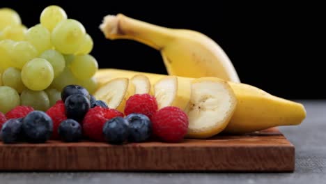 collection of fresh fruit on wooden cutting board, orange, grapes, raspberries, banana