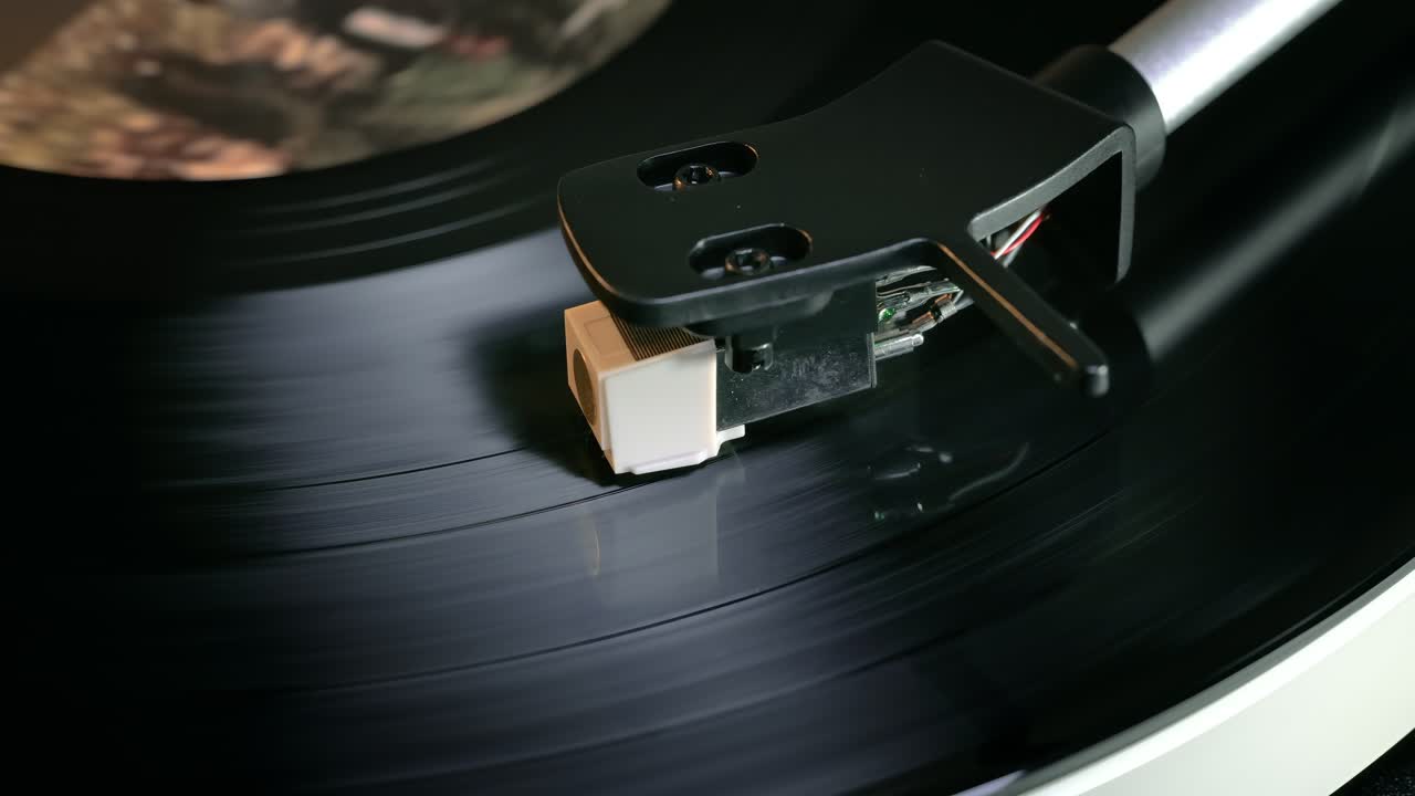 Primo piano dettagliato del braccio di un giradischi con testina bianca, posizionato su un disco in vinile nero sul piatto, che evidenzia la precisione delle apparecchiature audio