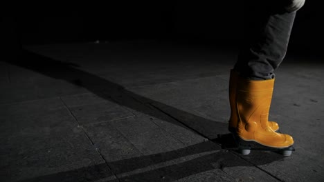 person walking in yellow rubber boots on a glass scale at night