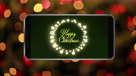 animation of happy christmas text with fairy lights on smartphone screen with out of focus light
