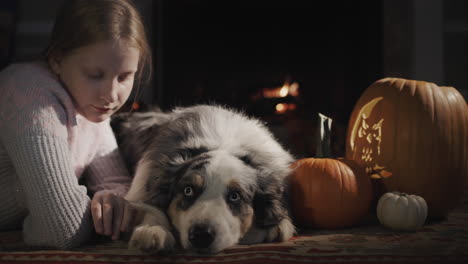 a child with a dog is resting by a burning fireplace, next to halloween decorations
