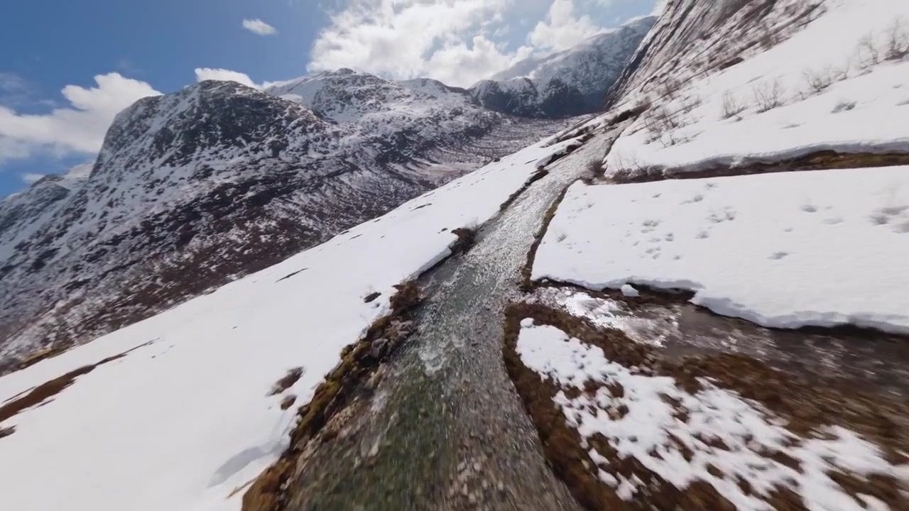 Low altitude drone shot flying fast along a river through a snow-covered mountain valley in Norway.