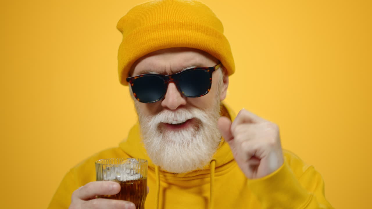 Munter eldre mann drikker juice i studio. Glad gammel fyr gleder seg innendørs.