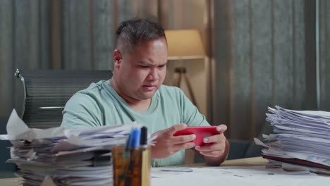 close up of fat asian man being upset losing game on smartphone after working with documents at the office