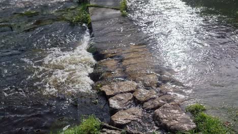 Rustic-stone-submerged-pathway-leading-to-arched-wooden-bridge-overflowing-from-flooded-river-in-Anglesey