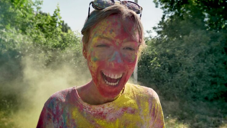 Young happy girl is thrown with yellow powder on holi festival in daytime in summer, laughing, color concept